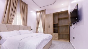 A bedroom with a bed, a wardrobe, and a TV mounted on the wall. - RHEMA APARTMENTS (Lagos)