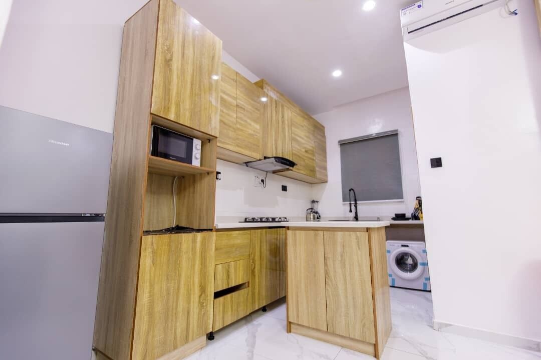 Una cocina moderna con armarios de madera, microondas integrado, un lavamanos y una lavadora al fondo.