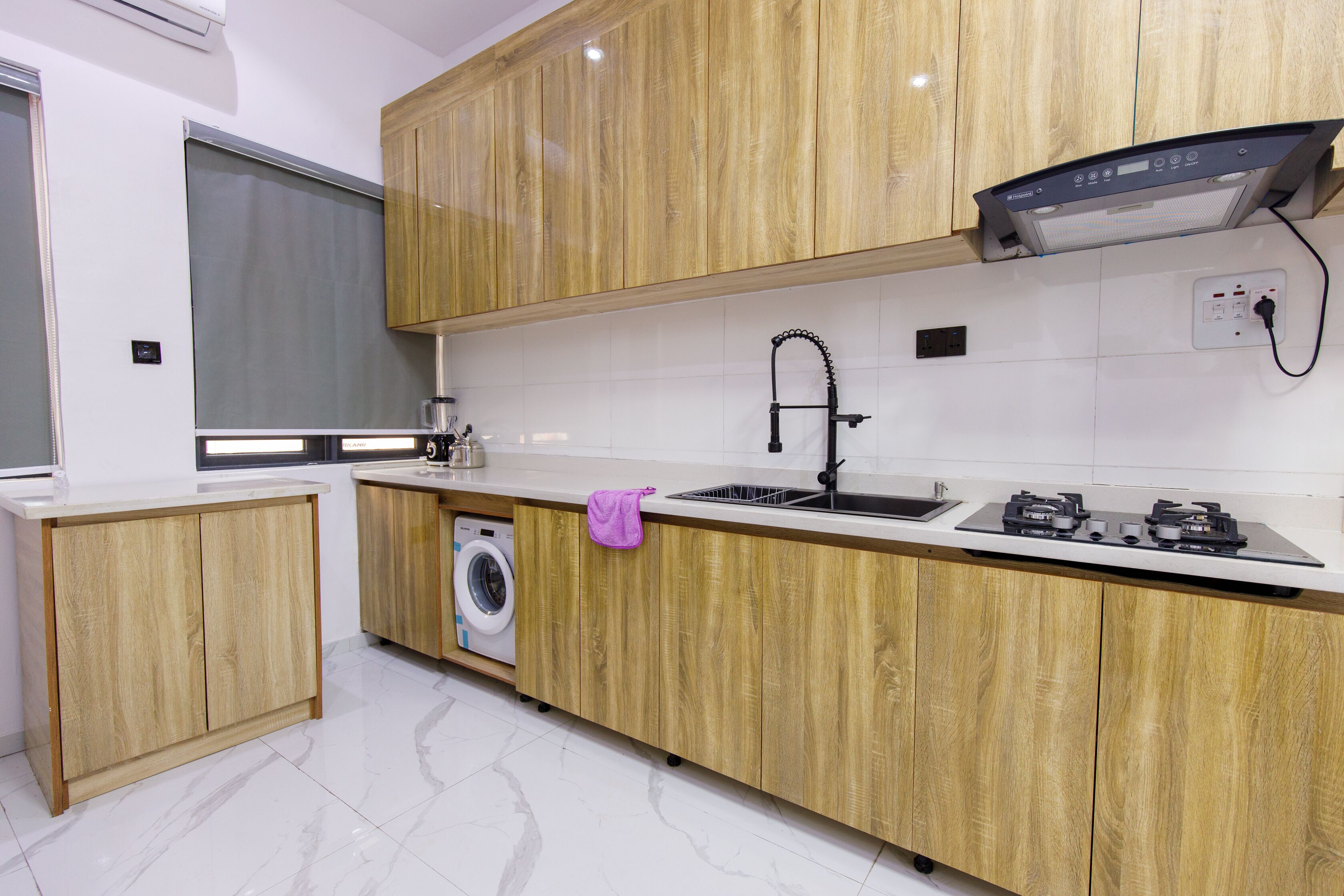A modern kitchen with wooden cabinets, a built-in washing machine, a stainless steel sink, and a gas stove.
