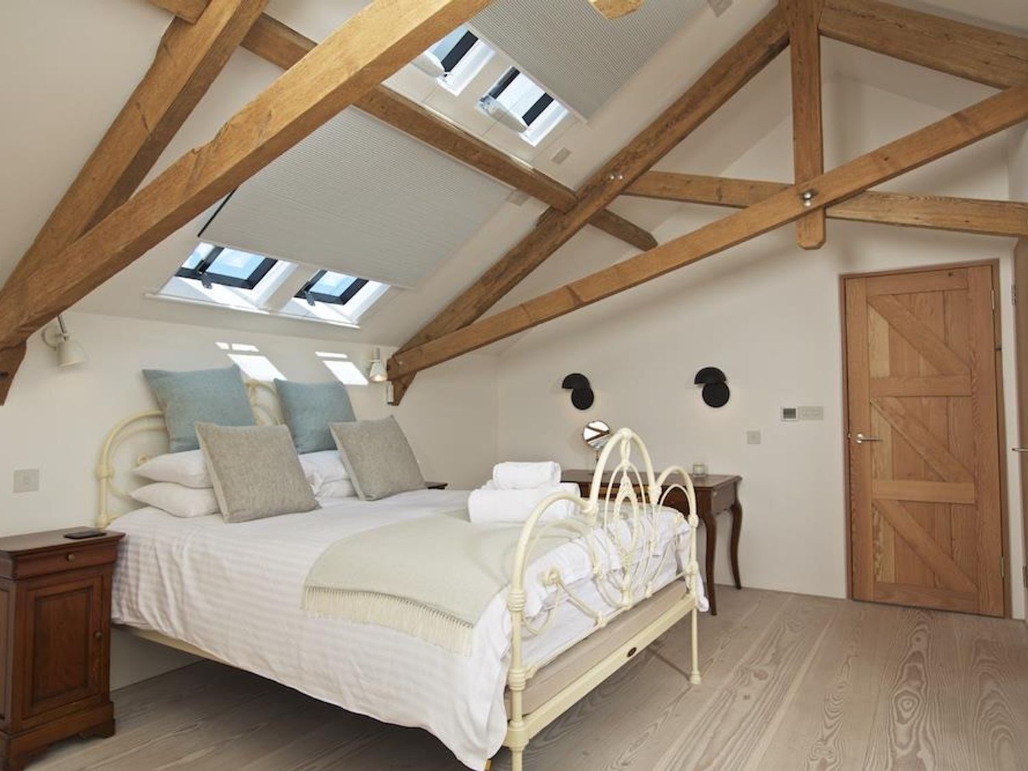 Un dormitorio con techo inclinado, cama, mesitas de noche y una puerta.