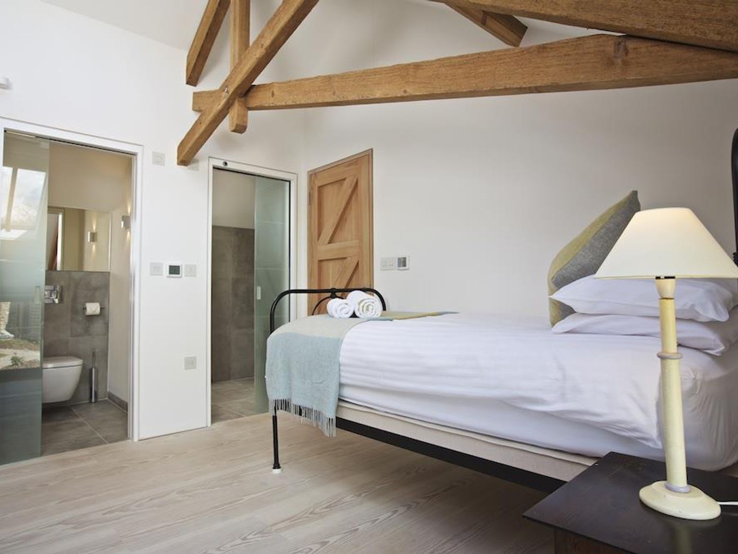 Una camera da letto con un letto, un comodino, una lampada e una trave in legno al soffitto.