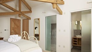 A bedroom with a bed, wooden beams, a wardrobe, a mirror, and a bathroom visible through a glass door.