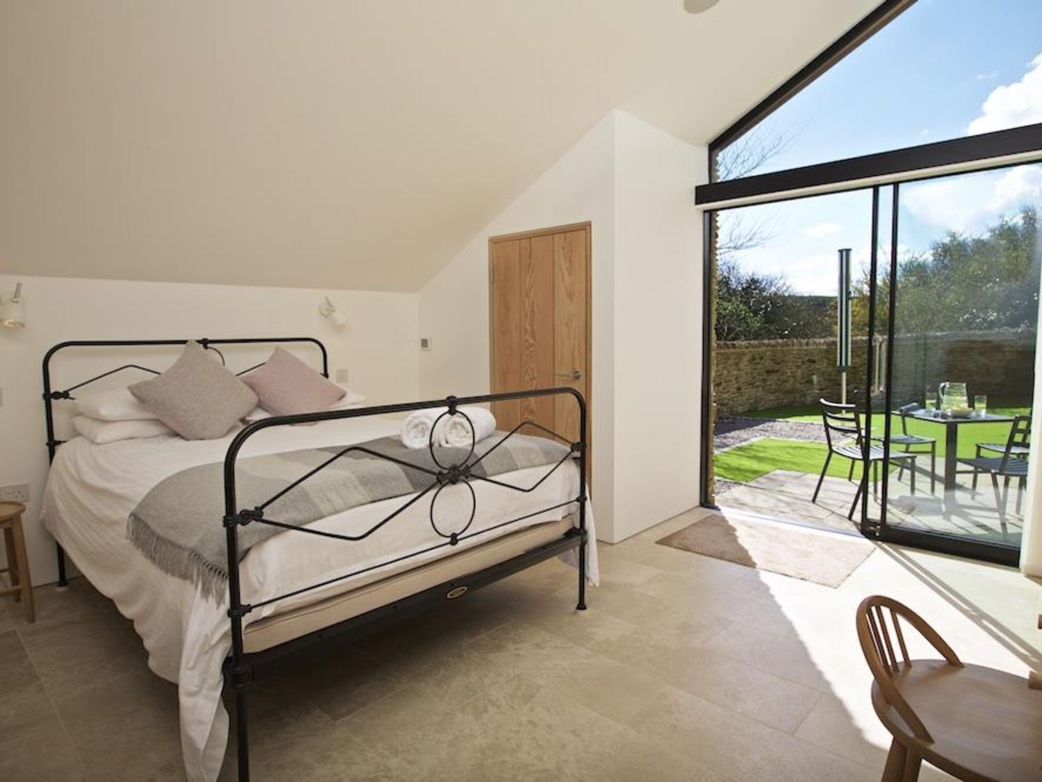 Ein Schlafzimmer mit Bett, einer Holztür und Blick auf eine Terrasse mit Gartenmöbeln.