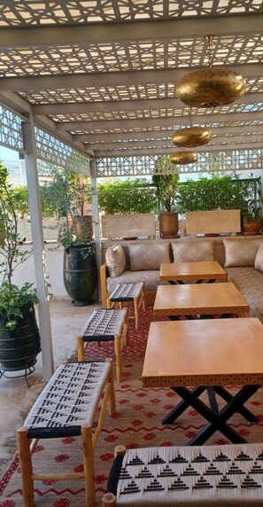A covered outdoor seating area with wooden tables and benches, potted plants, and a patterned floor. - RIAD CONTESSA, 6 magnificent suites in the best Medina neighborhood, Dar Bacha   (Marrakech)