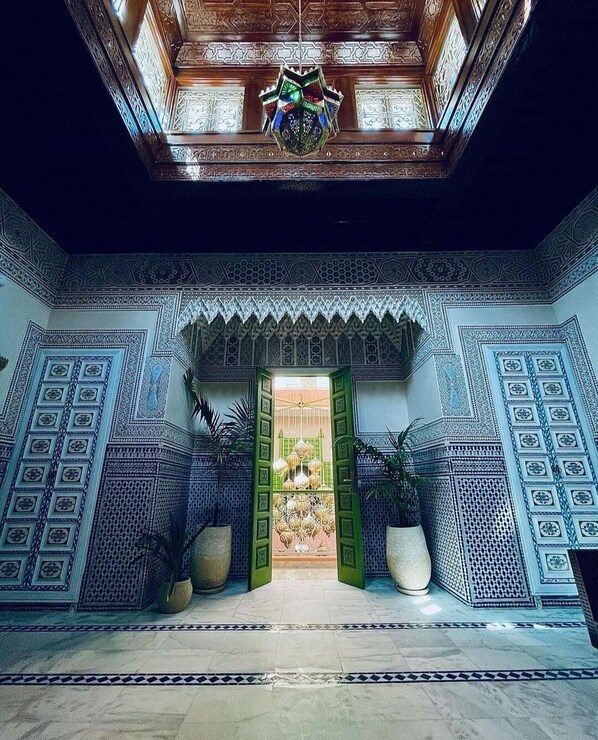An interior with a geometric patterned wall, a wooden ceiling with intricate designs, and a central doorway with green doors. - RIAD CONTESSA, 6 magnificent suites in the best Medina neighborhood, Dar Bacha   (Marrakech)