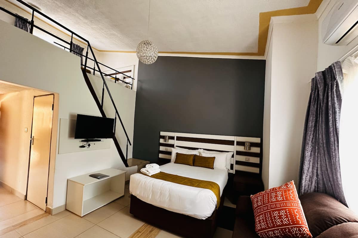 A bedroom with a bed, bedside table, TV, and a staircase.