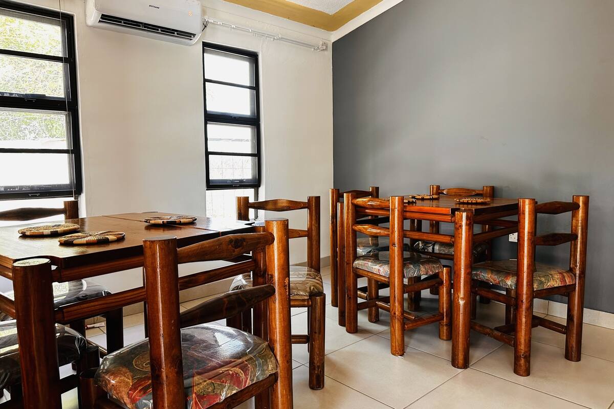 A dining area with a wooden table and chairs, a television on the wall, and large windows.