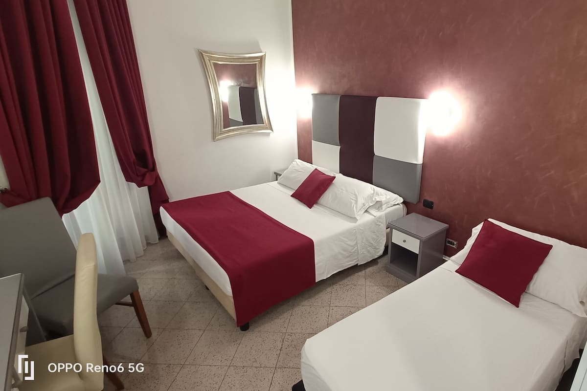 A hotel room with two beds, a nightstand, a mirror, and a red curtain.