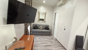 A modern living room with a flat-screen TV mounted on the wall, a grey sofa with patterned cushions, a wooden coffee table, and a patterned rug. - House Quattro Mori (Rome)