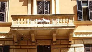 A building with a stone facade, a central entrance with a wooden door, and a balcony with a sign above it. - House Quattro Mori (Rome)