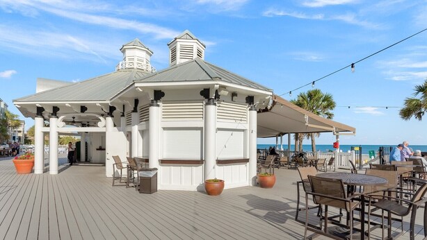 Un espace extérieur abrité, avec des tables et des chaises, donnant sur une plage.