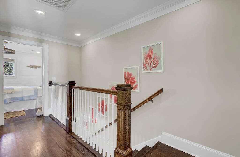 A staircase with a wooden handrail and white balusters, leading to a room with a bed and a window.