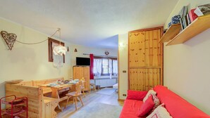 A cozy living room with a red sofa, wooden furniture, a TV, and a dining area.