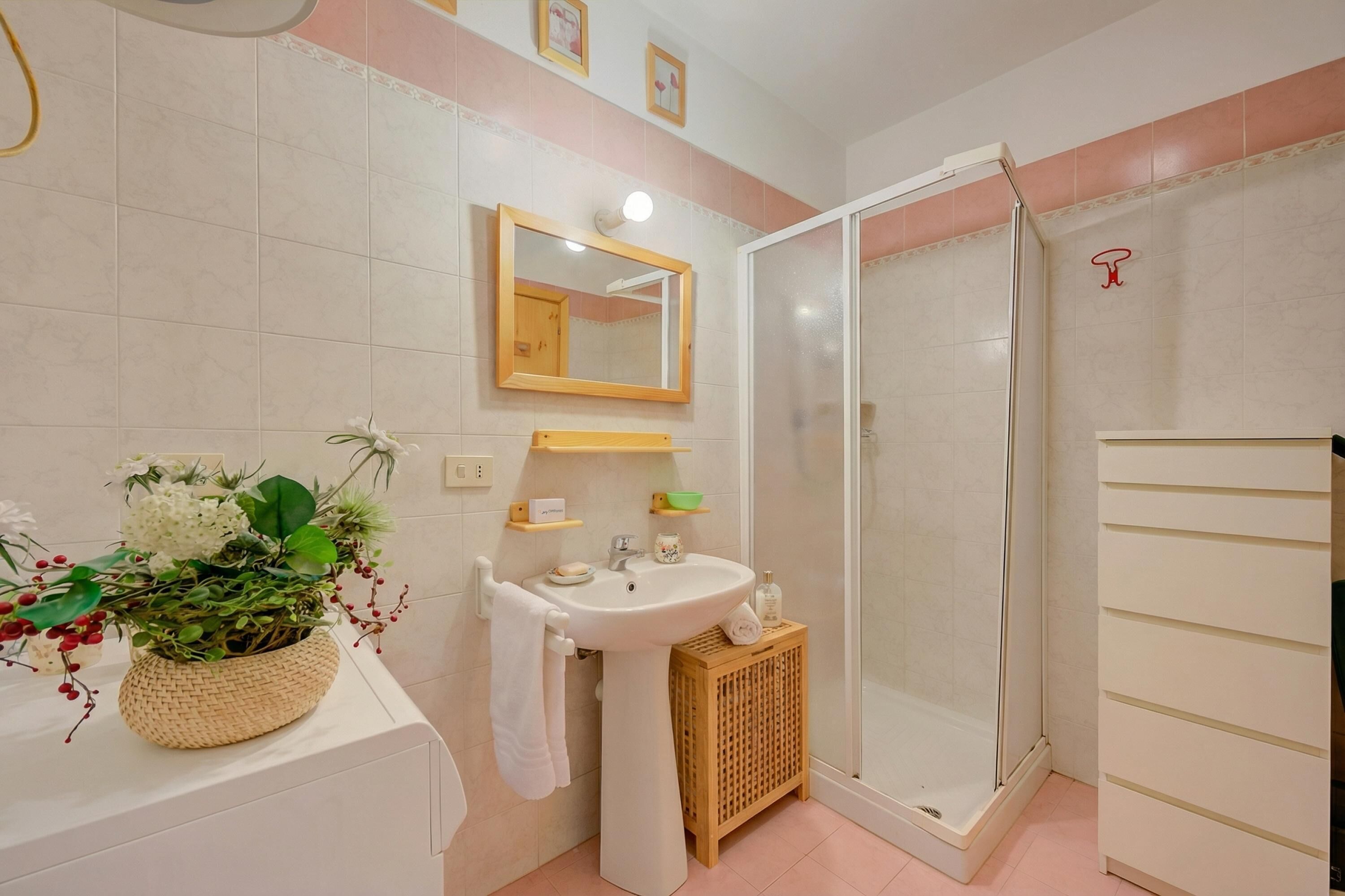 A bathroom with a sink, mirror, shower, and a decorative plant.