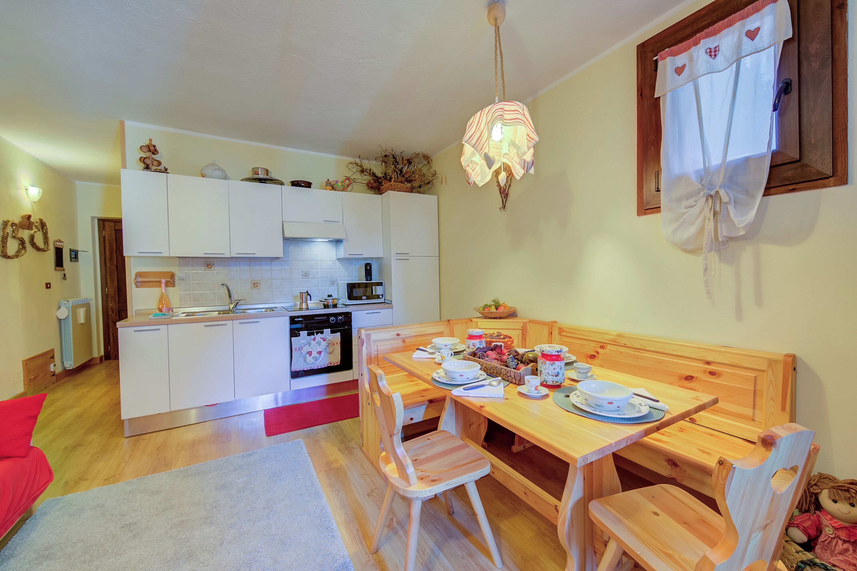 Una cucina compatta con mobili bianchi, un tavolo da pranzo in legno e un lampadario.