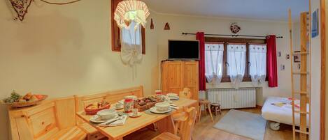 Una habitación acogedora con una mesa de madera para dos, televisión y una ventana con cortinas.
