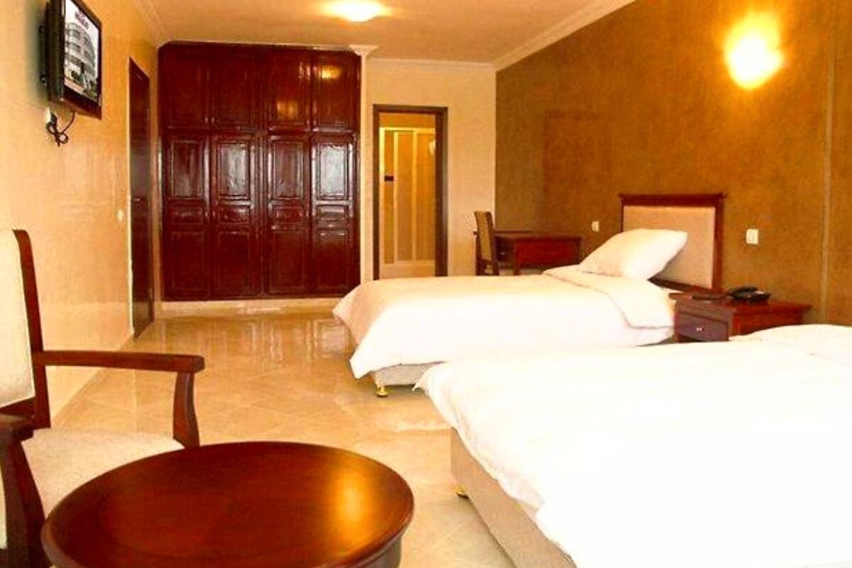 A hotel room with two beds, a wooden wardrobe, a small table, and a chair.