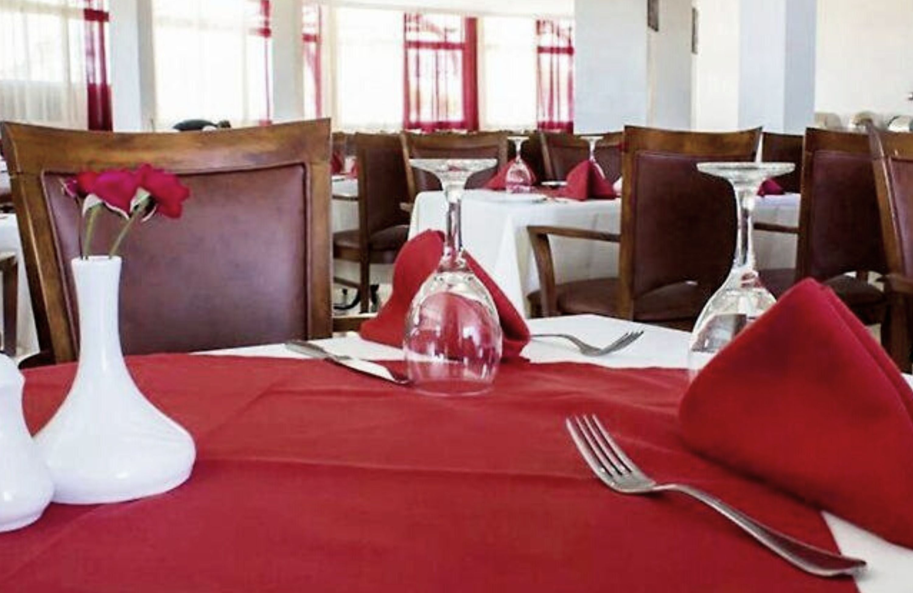 A dining table set with a red tablecloth, white vase with a red flower, and a clear glass dome.