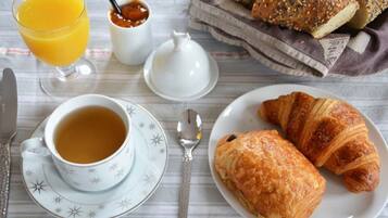 Una mesa con bollos de croissant, un vaso de zumo de naranja, una taza de té y un frasco pequeño de mermelada.