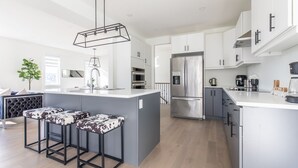 A modern kitchen with a central island, stainless steel appliances, and bar stools. - Comfortable Lux | Sleeps 10 | PingPong, Cozy Family Movie Room (London)