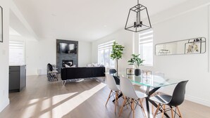 A modern living room with a glass dining table, black sofa, and a fireplace. - Comfortable Lux | Sleeps 10 | PingPong, Cozy Family Movie Room (London)