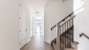 A hallway with white doors, a wooden staircase, and a view into another room. - Comfortable Lux | Sleeps 10 | PingPong, Cozy Family Movie Room (London)