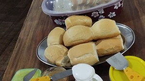 A wooden table with various food items including bread, a jar of honey, and a container of butter. - Pousada e Parada Colonial (Capitão Leônidas Marques)