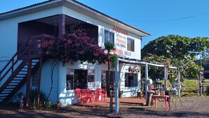 A building with a staircase leading to a covered entrance, a signboard with contact information, and outdoor seating with red chairs. - Pousada e Parada Colonial (Capitão Leônidas Marques)