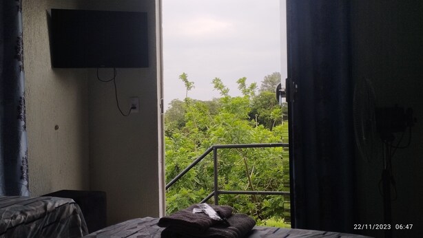 A room with a bed, a TV mounted on the wall, and a window with a view of greenery. - Pousada e Parada Colonial (Capitão Leônidas Marques)