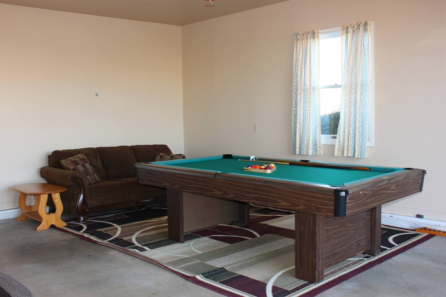 A pool table in a room with a brown sofa and a small wooden stool.