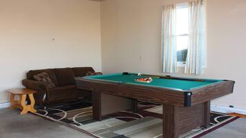 A pool table in a room with a brown sofa and a small wooden stool.