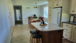 A spacious kitchen with a large island, wooden stools, and a refrigerator. - Homestead Guesthouse (Honey Brook)