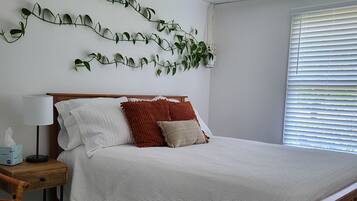 A neatly made bed with white bedding, a wooden headboard, and decorative pillows. A bedside table with a lamp and a tissue box is visible.