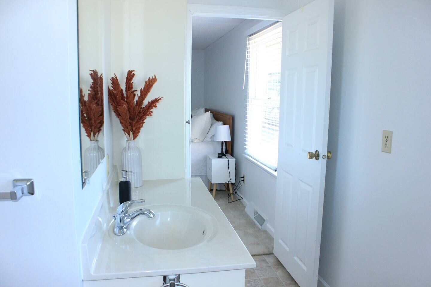 Un baño con un lavabo blanco, un espejo y una puerta que da a un dormitorio.