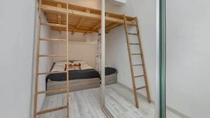 Een kleine kamer met een enkel bed, een houten trapje en een spiegeldeur kast.