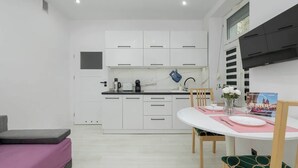 Een moderne keuken met witte kastjes, een zwart aanrecht en een eethoek met een witte tafel en stoelen.