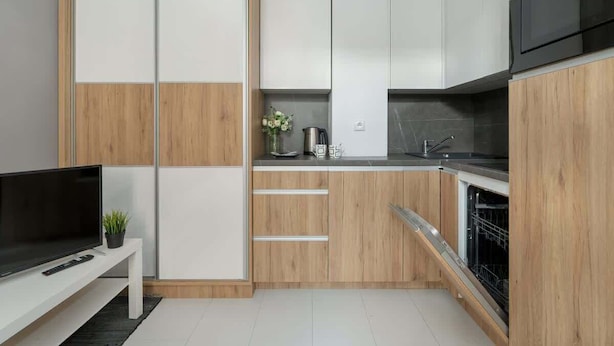 Una cucina moderna con mobili bianchi e in legno, un forno integrato e un piccolo piano di lavoro con bollitore e fiori.