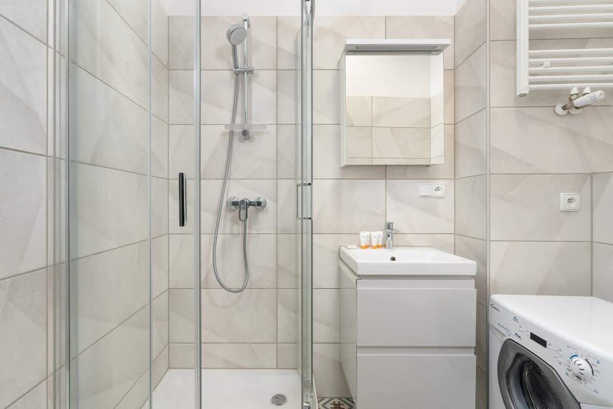Un baño moderno con ducha de vidrio, lavabo con artículos de aseo y lavadora.