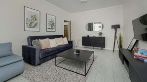A modern living room with a dark blue sofa, a coffee table, and a TV on a stand.