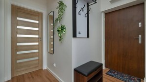 A hallway with a wooden door, a bench, a mirror, and a plant.