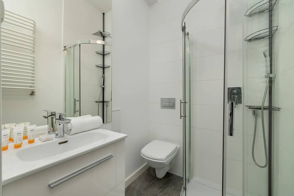 Et moderne badeværelse med en glasvægs brusekabine, et hvidt toilet og en vask med toiletartikler.