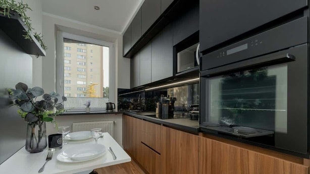 A modern kitchen with dark cabinetry, a built-in oven, and a dining area with a white table and chairs.