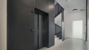 Um corredor moderno com um elevador fechado, uma escada e uma porta com sinal de saída de emergência.