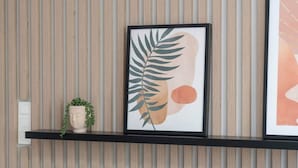 Obra emoldurada com folha e formas abstratas sobre uma prateleira fixada na parede.