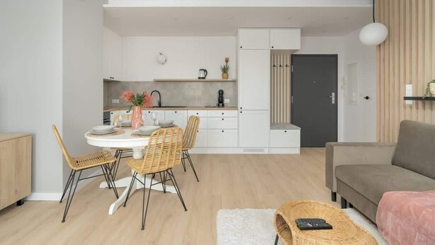 Uma sala de estar moderna com sofá, mesa de jantar com cadeiras e área de cozinha com armários e bancada.
