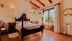 A bedroom with a four-poster bed, a nightstand, a chair, a window with curtains, and a view of the outdoors. - Son Cladera Bosch by Rentallorca (Manacor)