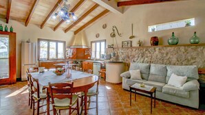 A spacious kitchen with wooden beams, a dining table with chairs, a sofa, and a stone wall. - Son Cladera Bosch by Rentallorca (Manacor)