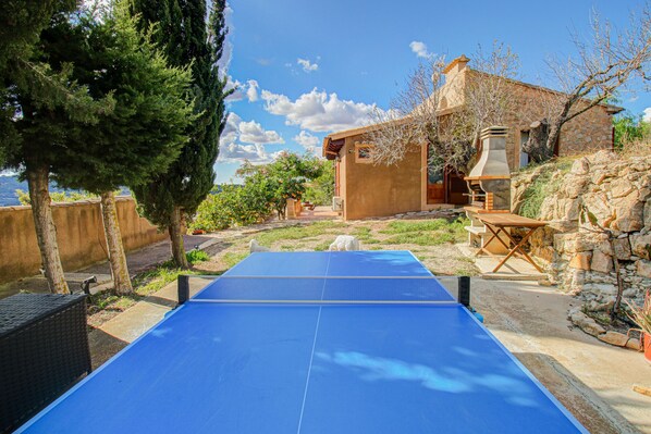 A ping pong table in a backyard with a stone house, trees, and a view of the sea. - Son Cladera Bosch by Rentallorca (Manacor)