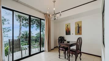A dining area with a table and chairs, a chandelier, and a view of the outdoors through large windows.