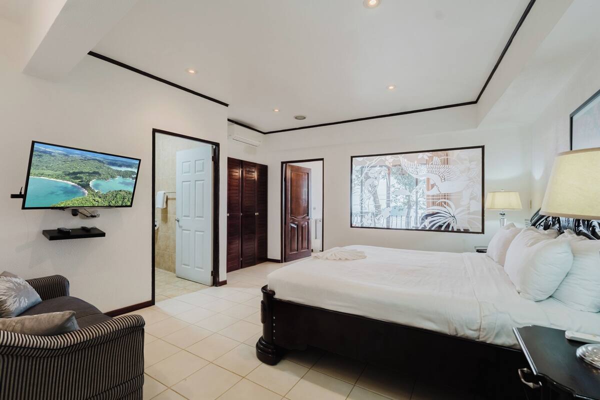 A hotel room with a large bed, a TV mounted on the wall, a sofa, and artwork on the walls.